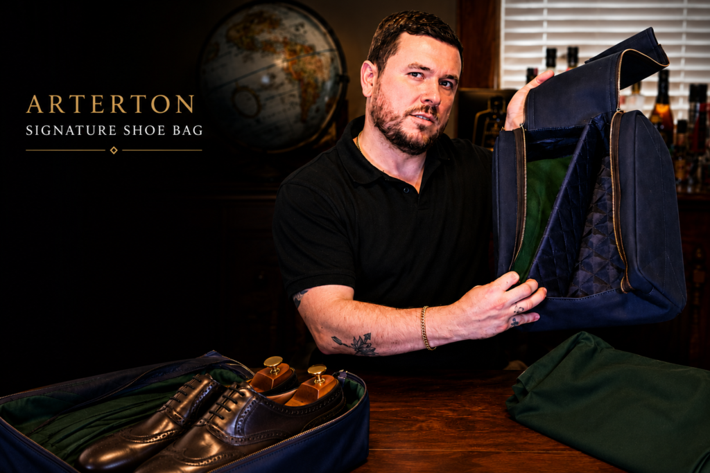 A man in a black shirt holds an open navy blue shoe bag, showcasing its green interior and a pair of brown dress shoes inside.